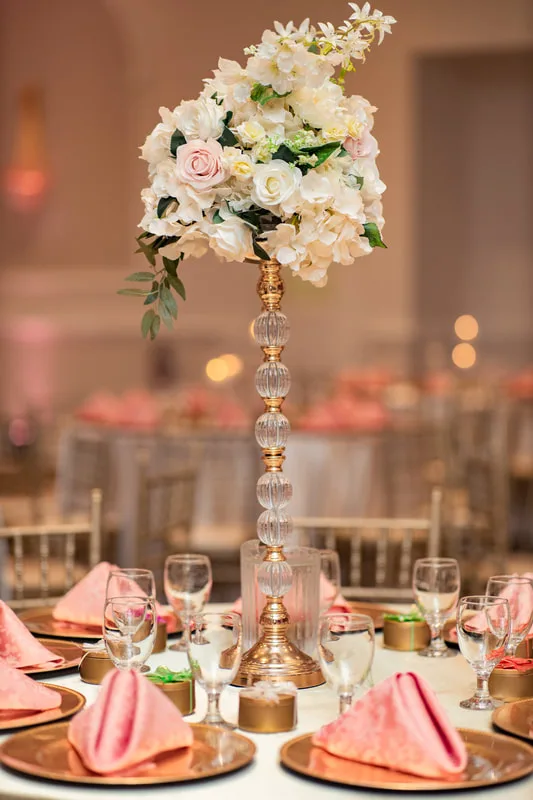 Tall crystal centrepiece with blush roses above gold chargers and pink napkins