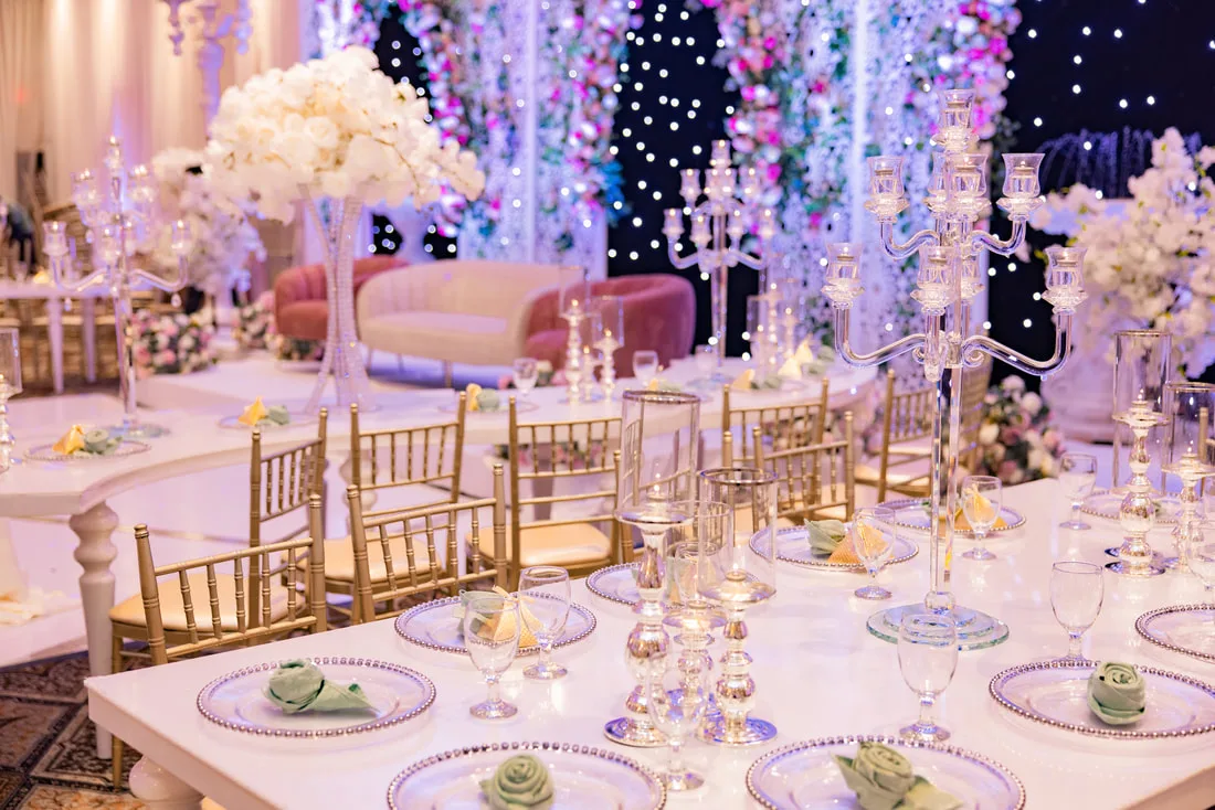 Gold-rimmed place settings with folded rose napkins and crystal candelabras